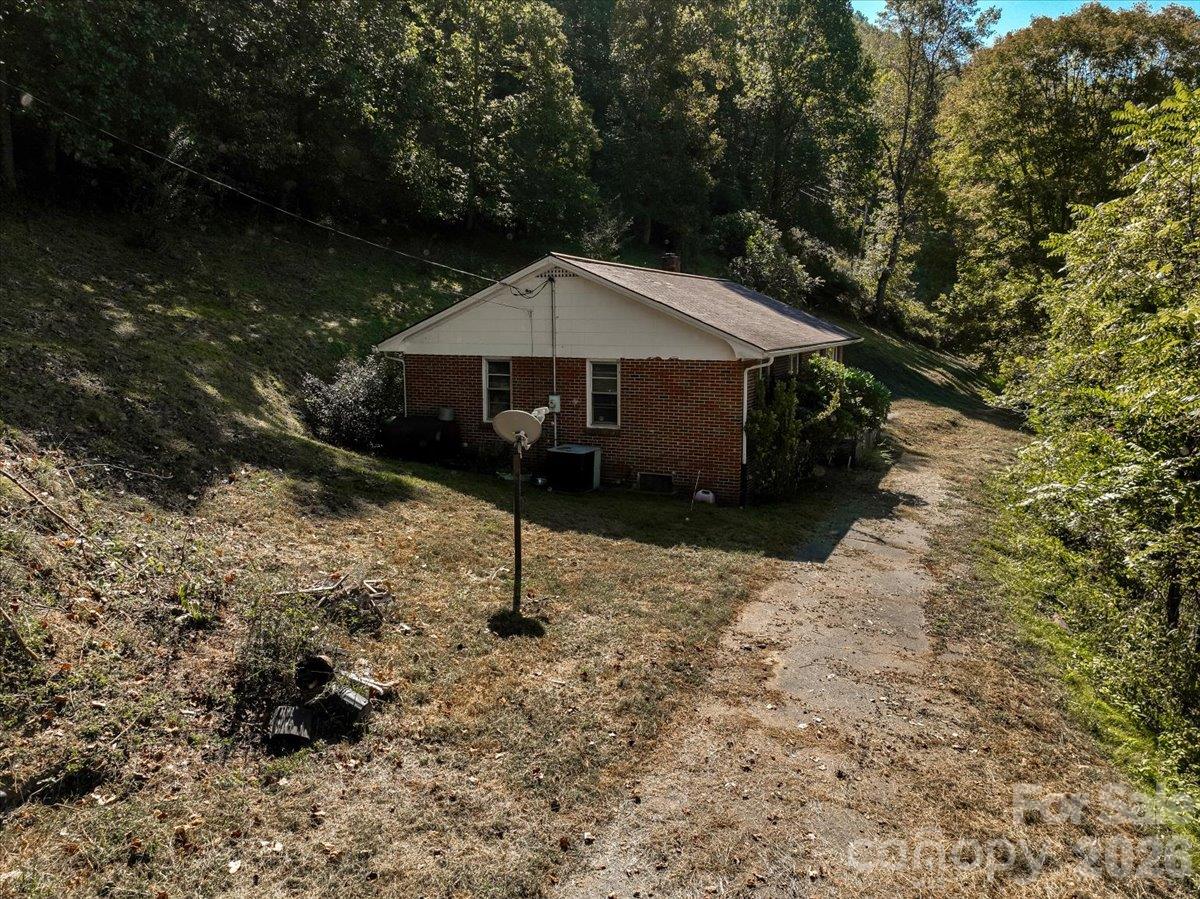Brick house on a wooded slope beside a narrow paved driveway and satellite dish.