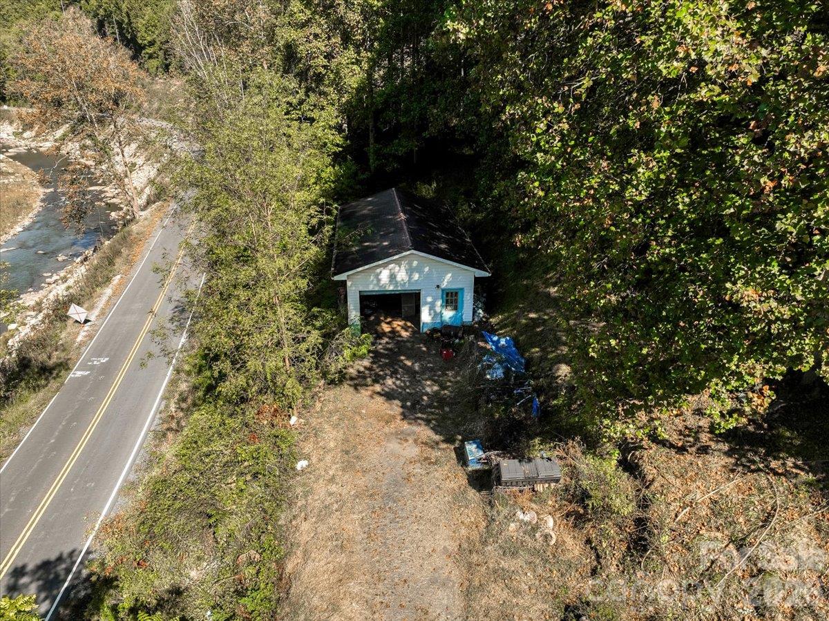 Aerial view of a small blue building beside a highway and creek, surrounded by autumn woods.
