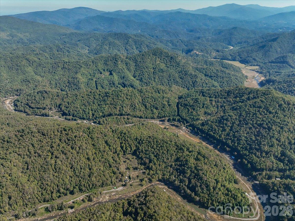 Aerial view of a wooded mountain valley with a winding river and distant ridges.