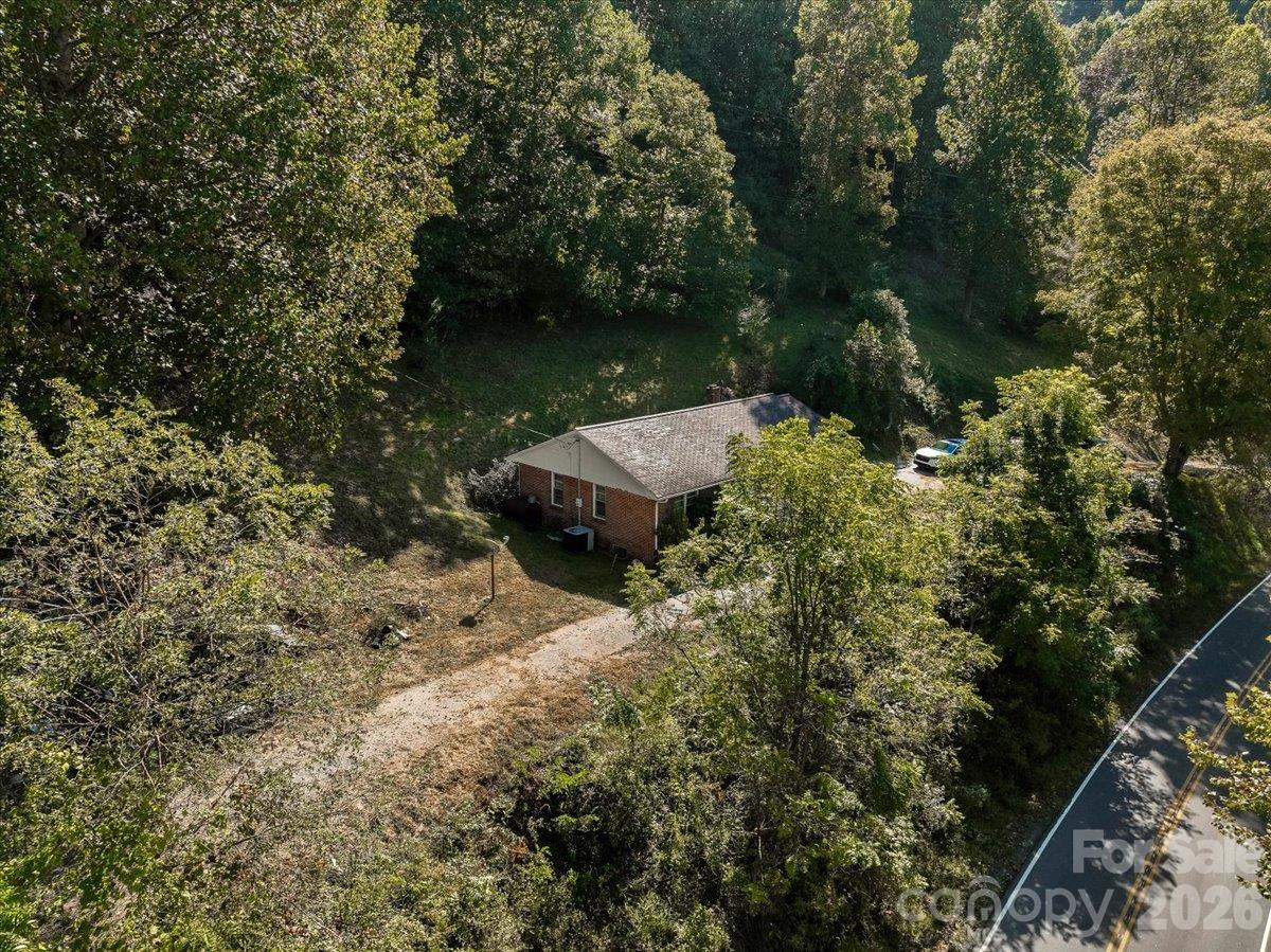 Aerial view of a brick house surrounded by trees, with a driveway beside the highway.