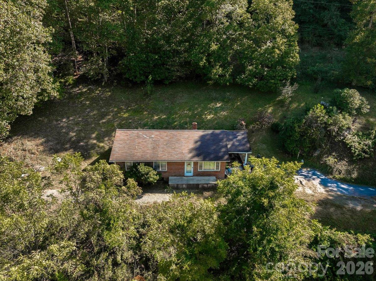 Aerial view of a brick ranch amid trees, with a broad grassy yard and driveway.