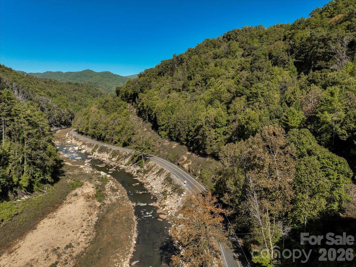 Aerial view of a wooded mountain road winding beside a rocky creek.