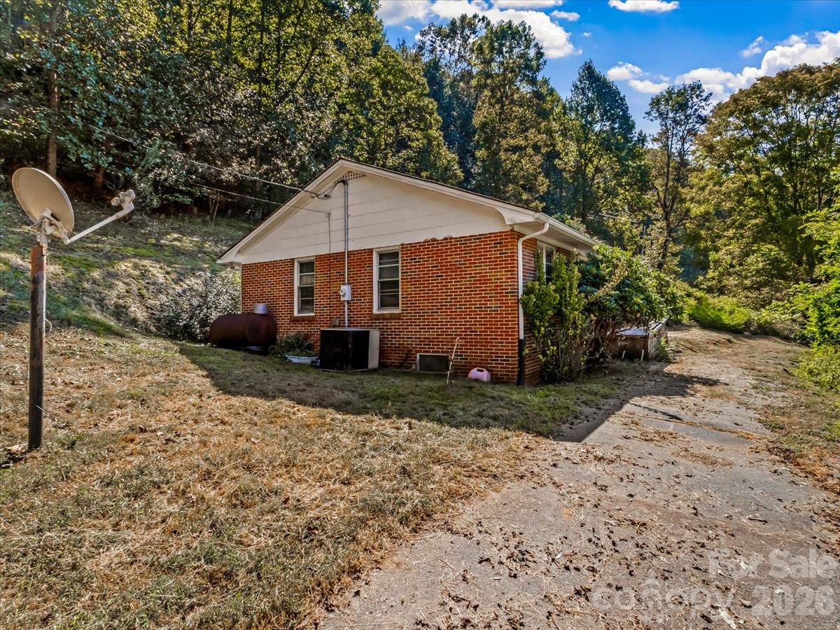 Red-brick house beside a wooded hillside, with a satellite dish and paved driveway.