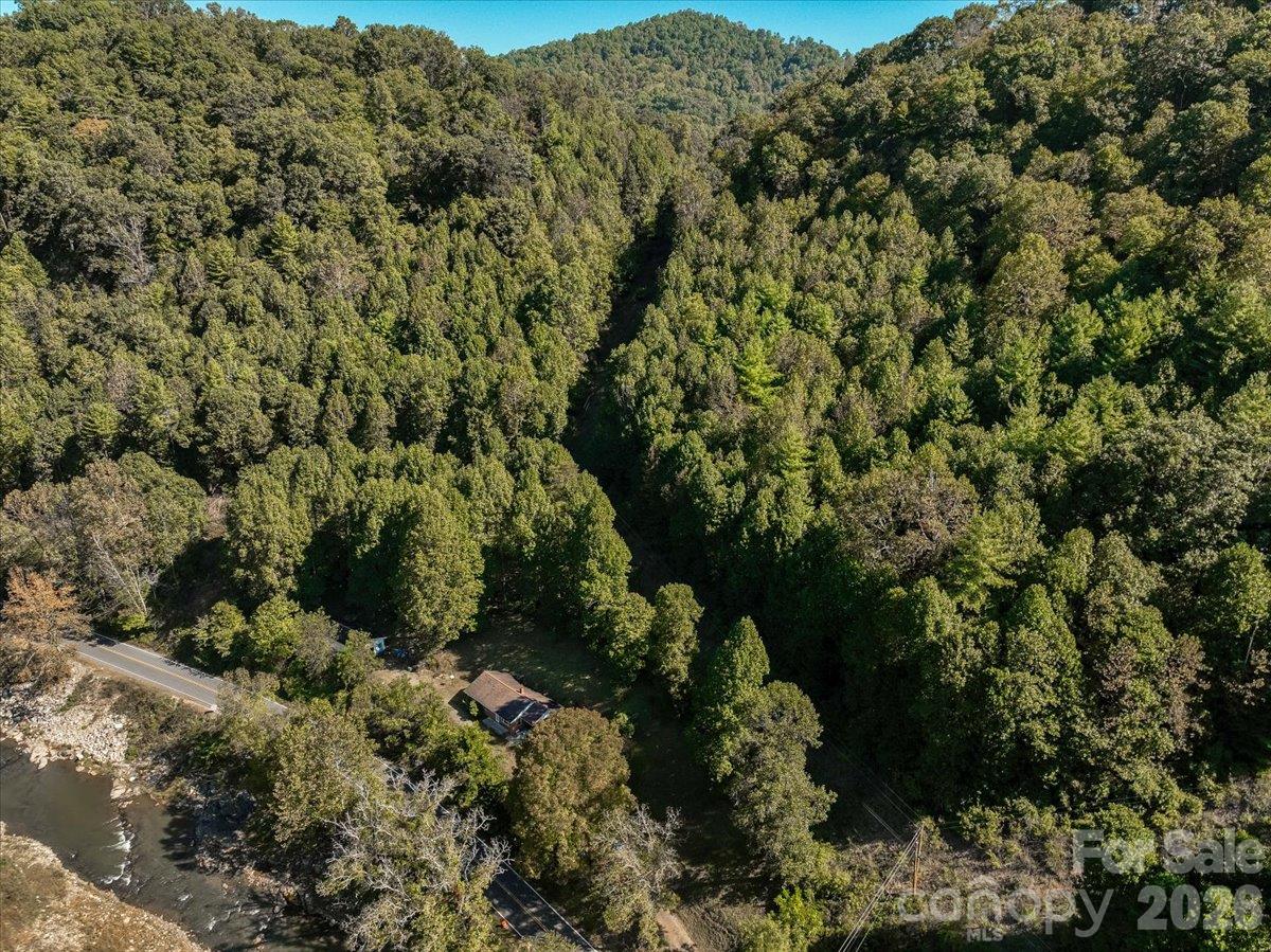Wooded property with a small house, road frontage, and creek amid forested hills.