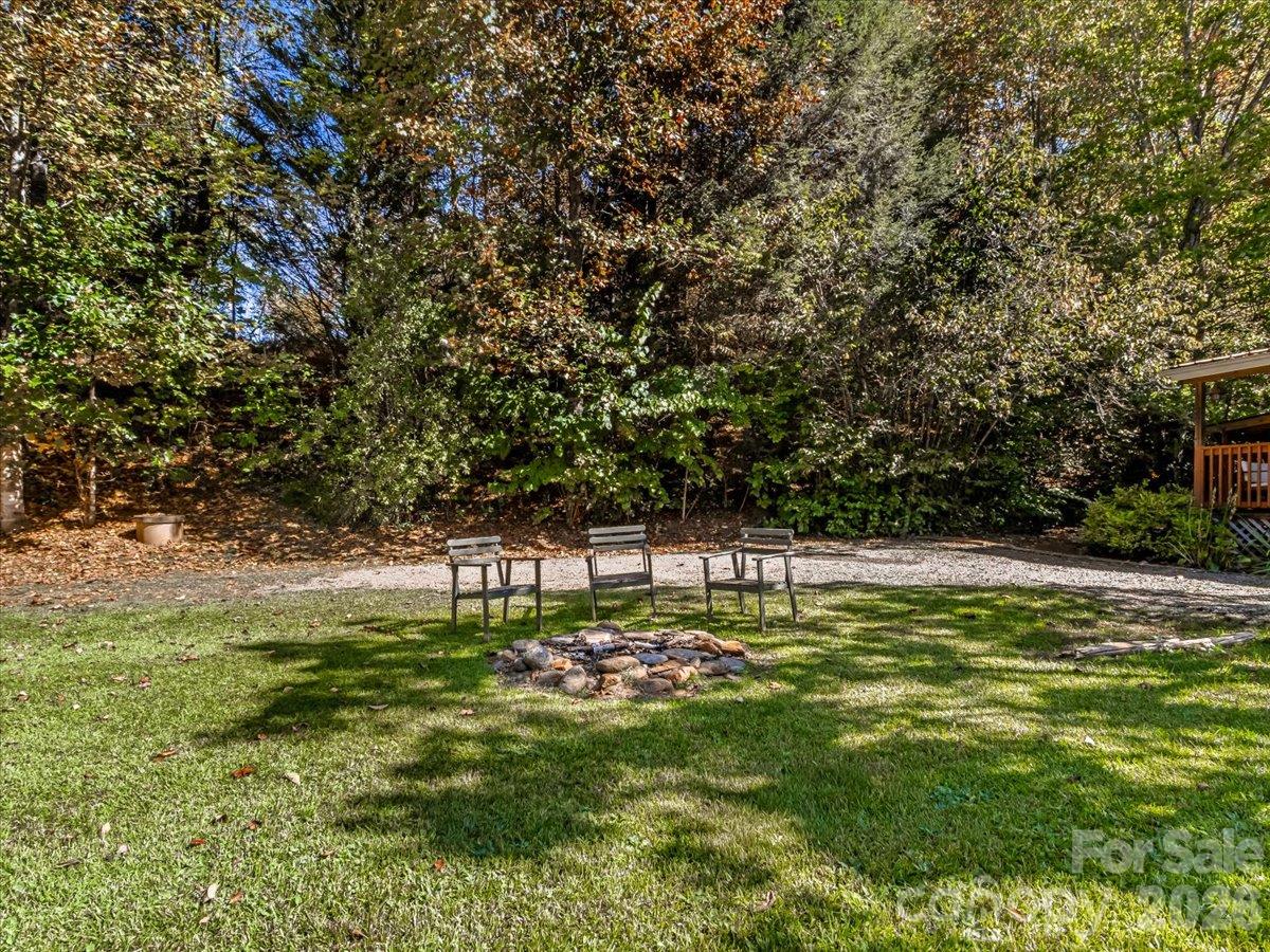 Wooded backyard with three chairs around a stone fire pit and a gravel seating area.