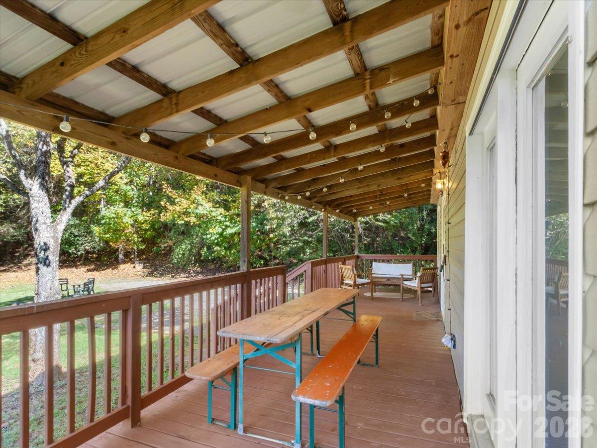 Covered wooden deck with exposed beams, string lights, picnic table, and wooded yard.