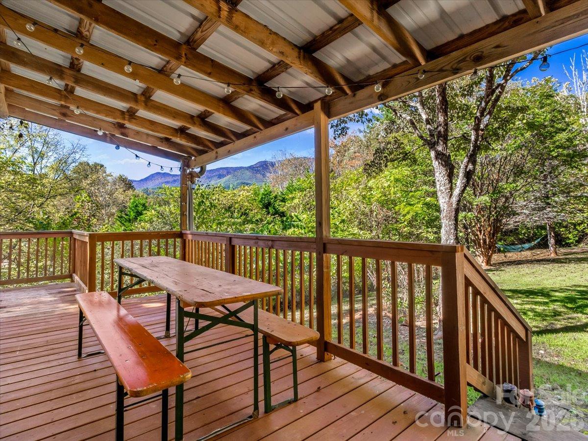 Covered wooden deck with a picnic table and mountain views beyond the trees.