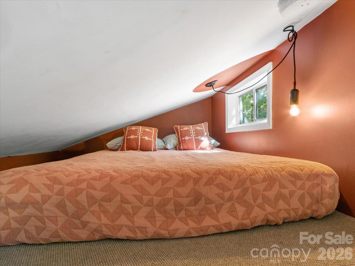 Attic bedroom with a large geometric-quilted bed, sloping ceiling, rust-colored walls, and a small window.