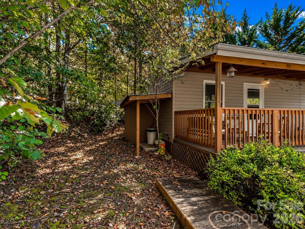 House with a covered wooden porch beside a leaf-covered path in a wooded yard.