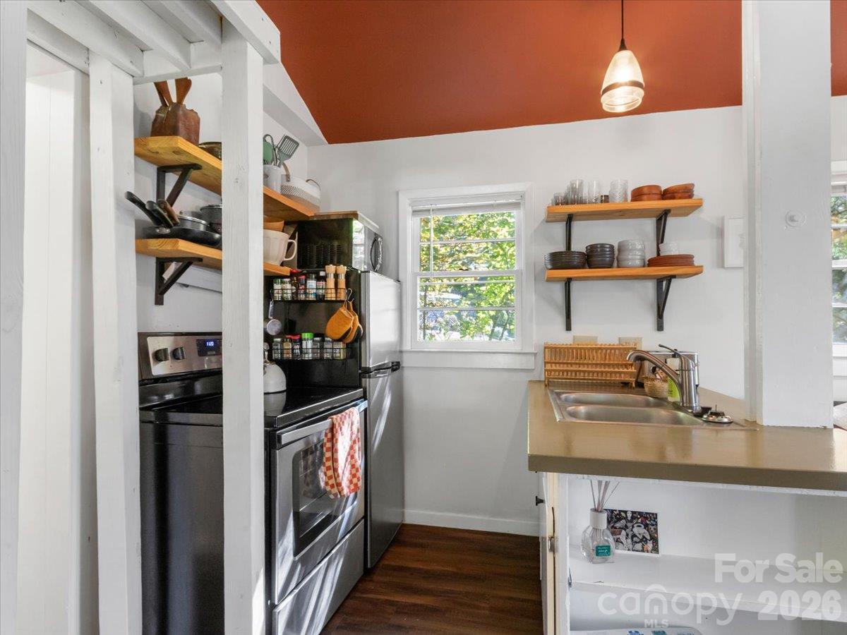 Kitchen with stainless steel appliances, open wooden shelves, and a sink counter beneath a terracotta ceiling.