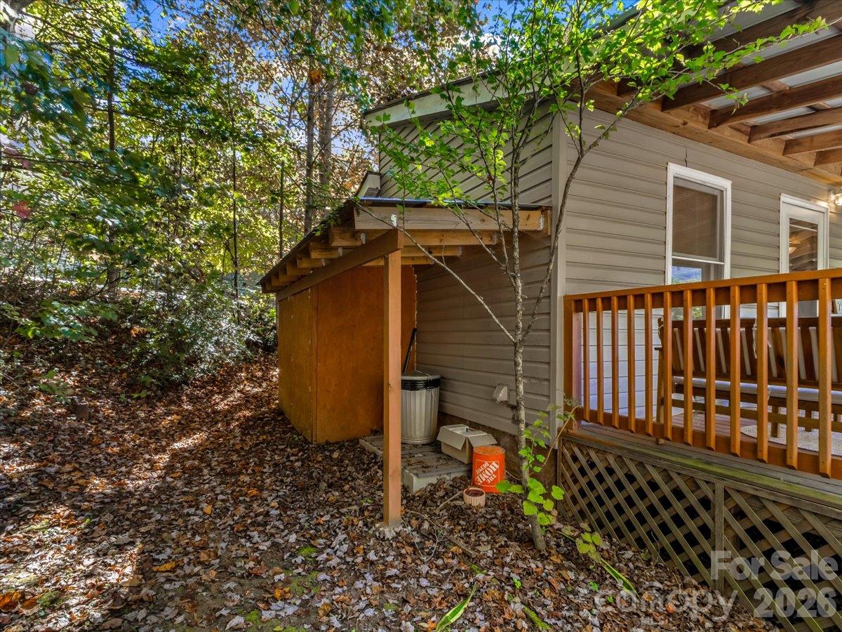 House exterior with a raised wooden deck, small shed, and wooded, leaf-covered yard.