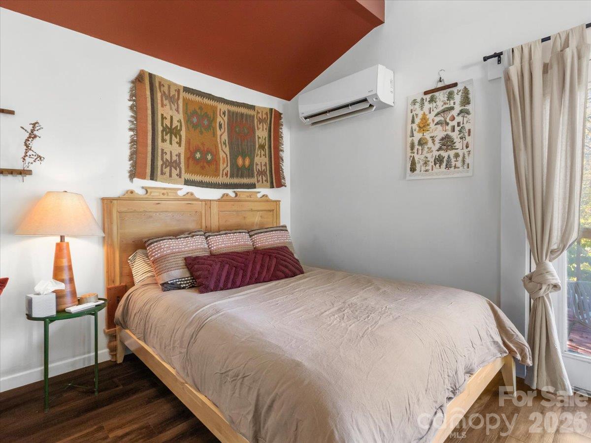 Bedroom with a wooden bed, patterned pillows, woven wall hanging, and wall-mounted air conditioner.