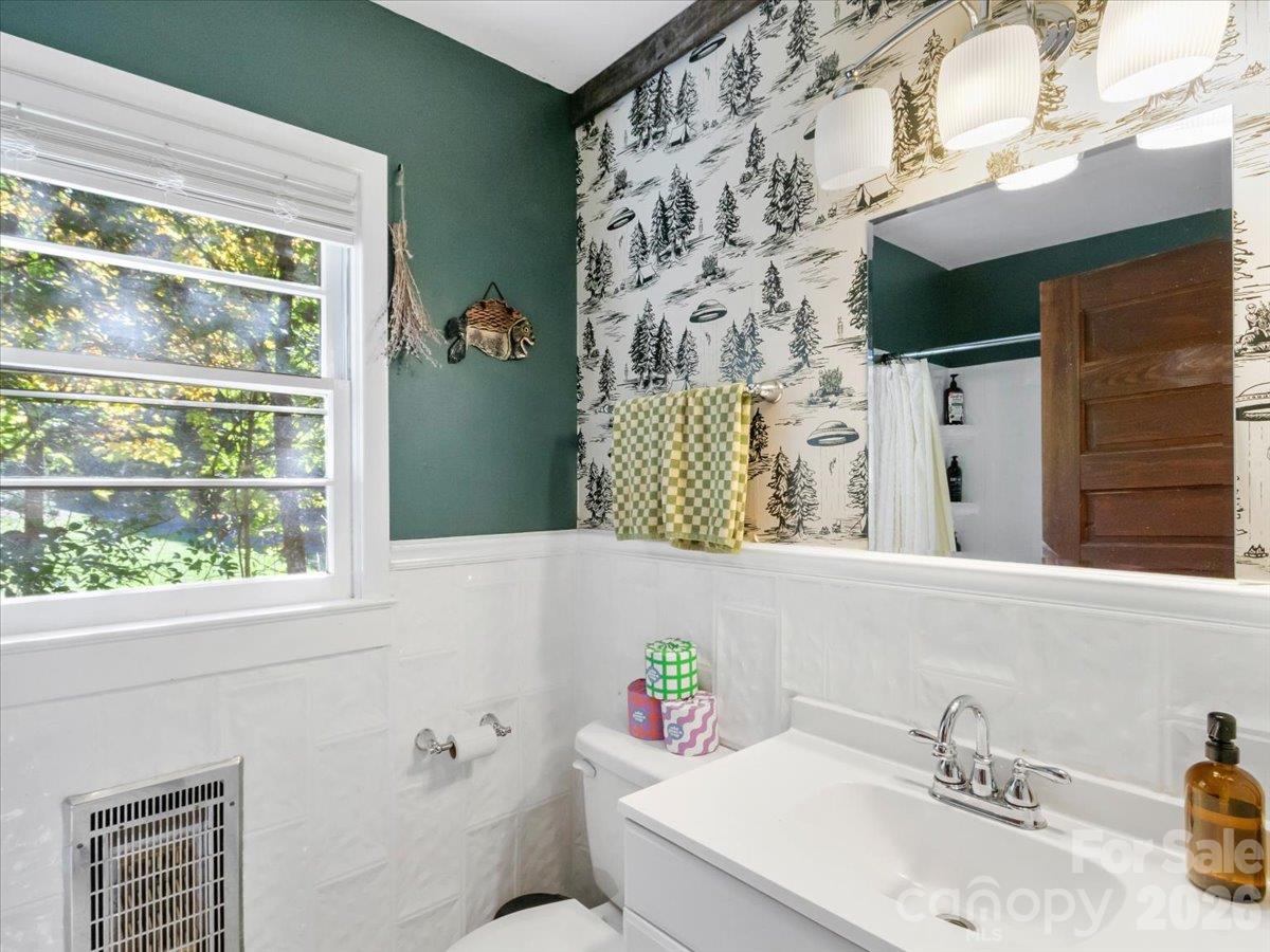 Bathroom with forest-patterned wallpaper, a white vanity, and a large window overlooking trees.