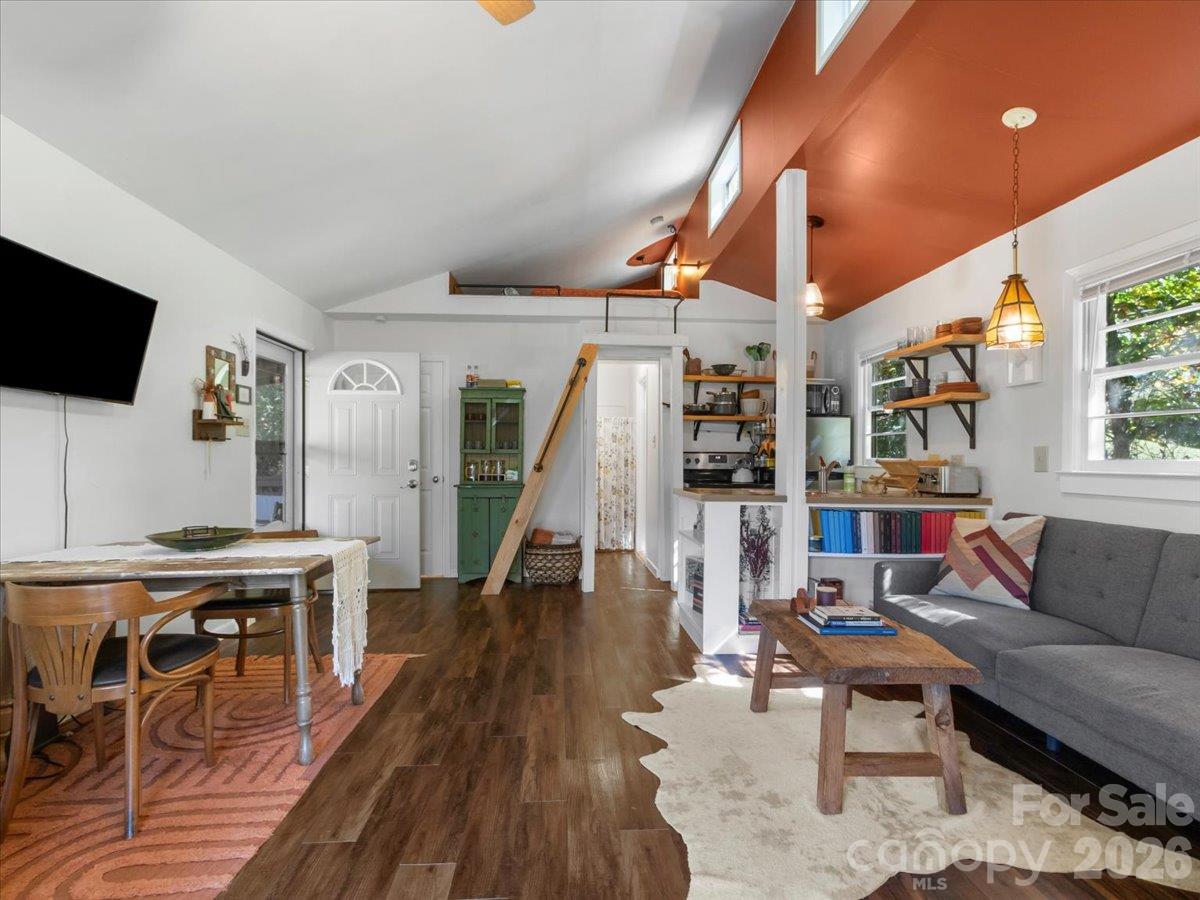 Open-plan living room with gray sectional, dining table, and vaulted ceiling with rust-colored accent.
