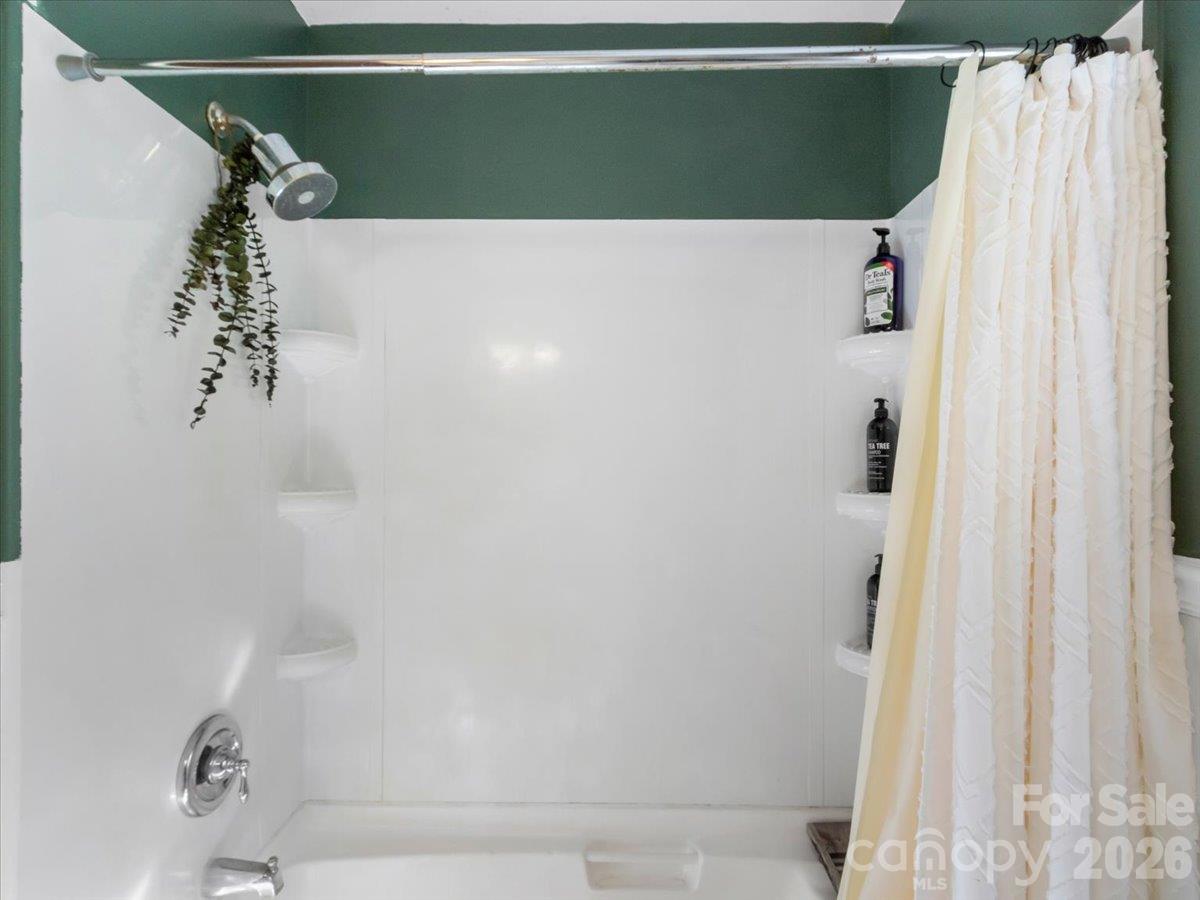 White bathtub and shower with a chrome showerhead, corner shelves, and a white curtain.