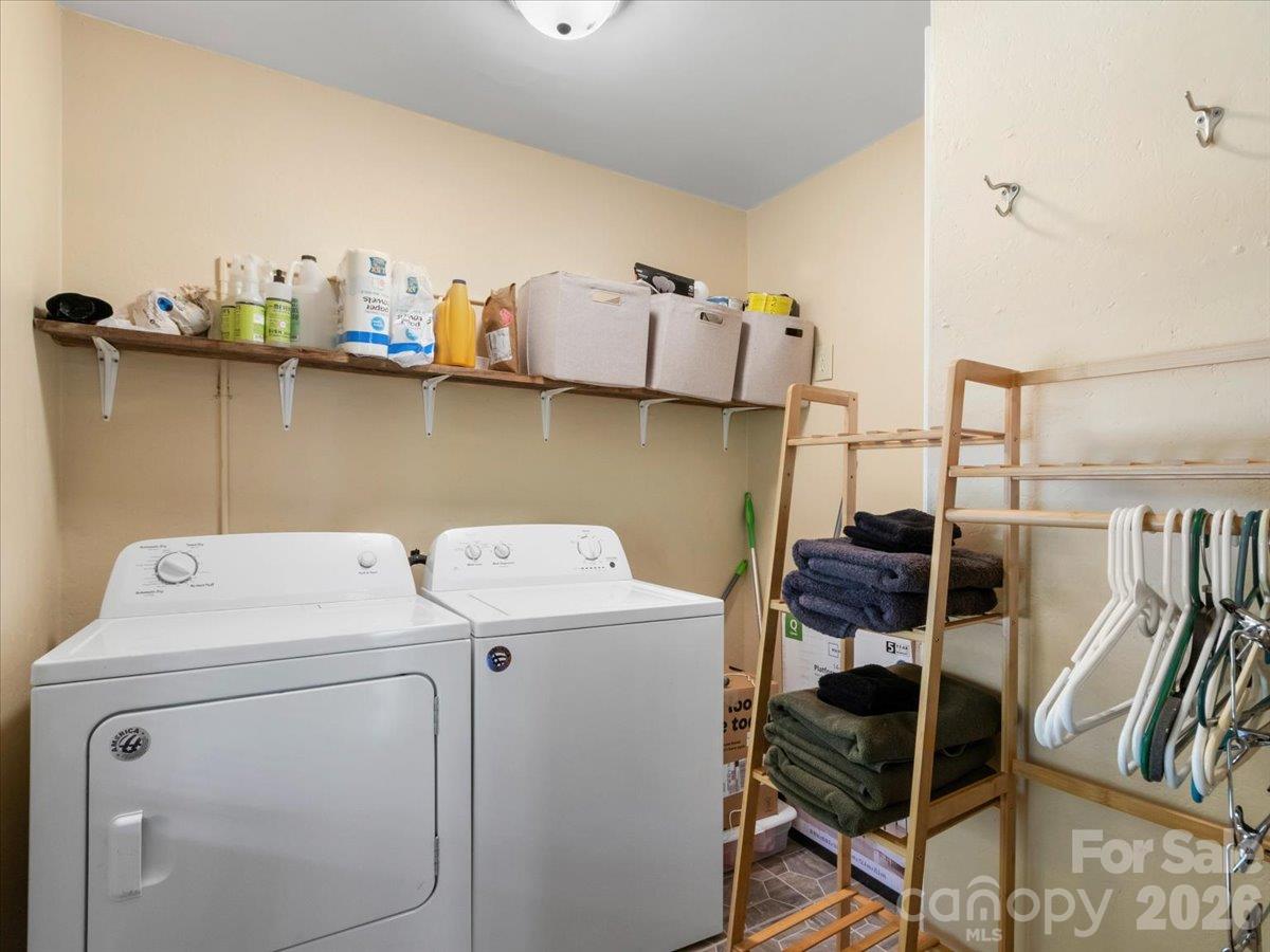 Laundry room with white washer and dryer, storage shelves, folded towels, and a rack of hangers.
