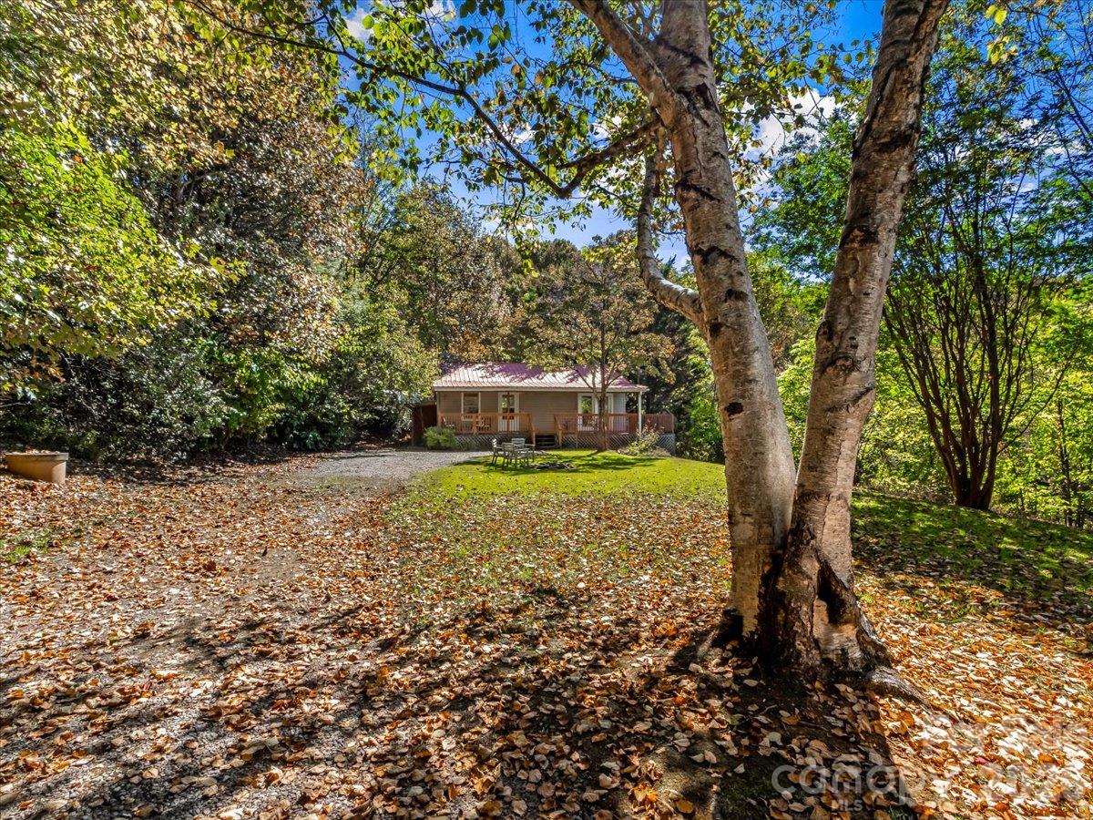 Single-story home with a covered porch, gravel drive, and wooded autumn yard.
