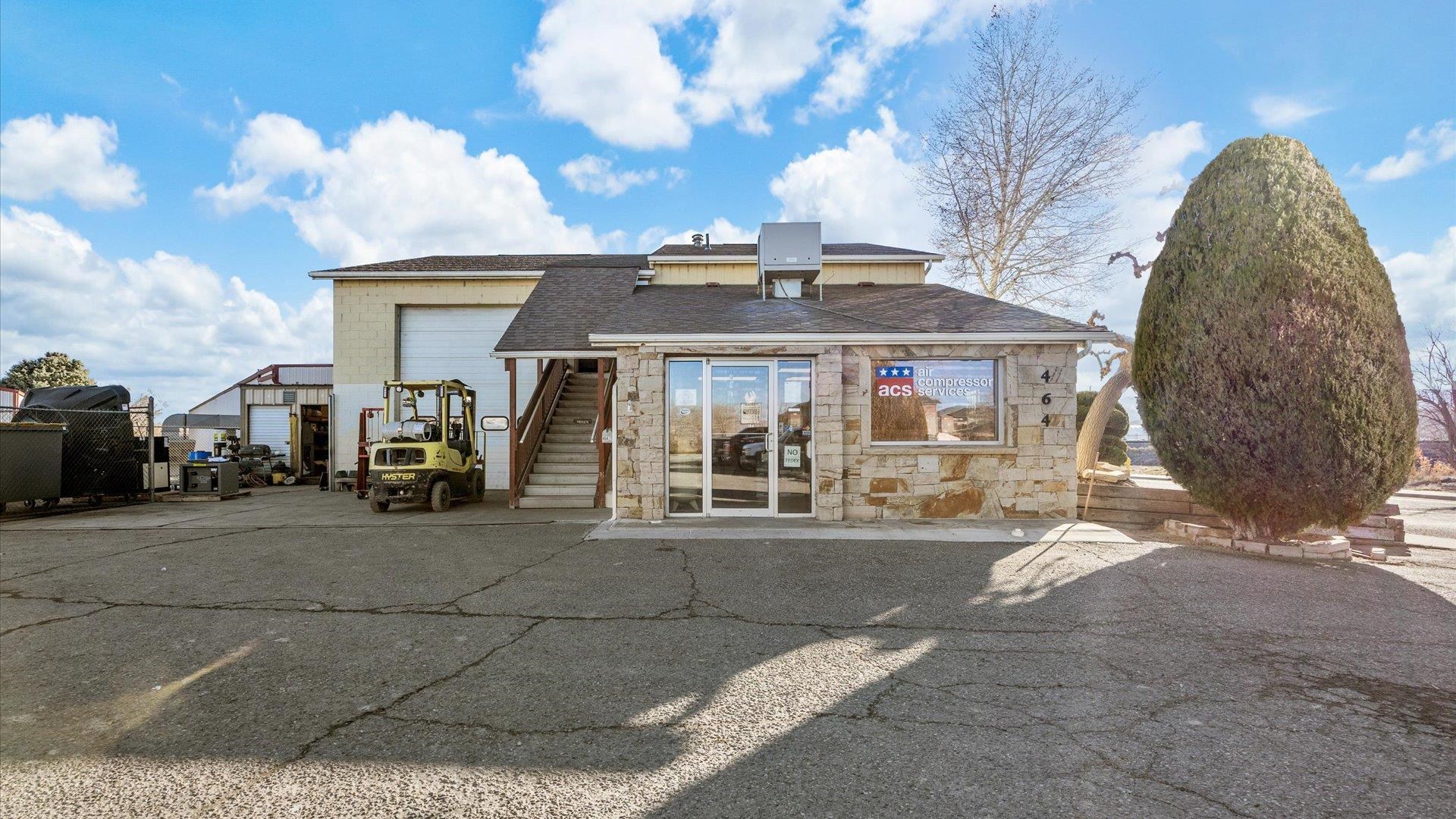 Commercial property with a stone-front office, attached industrial building, and forklift in the paved lot.