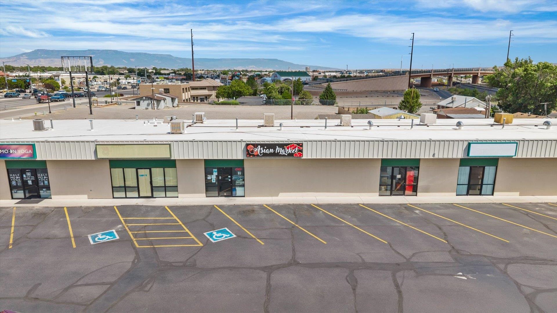 Commercial storefront strip with marked parking, Asian Market sign, and mountains in the distance.