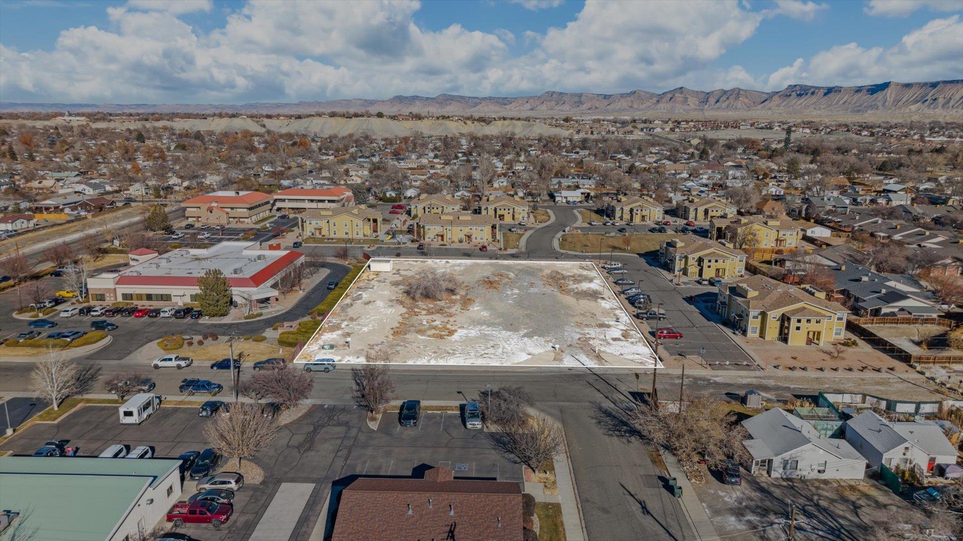 Vacant parcel outlined from above among nearby buildings, with mountains in the distance.