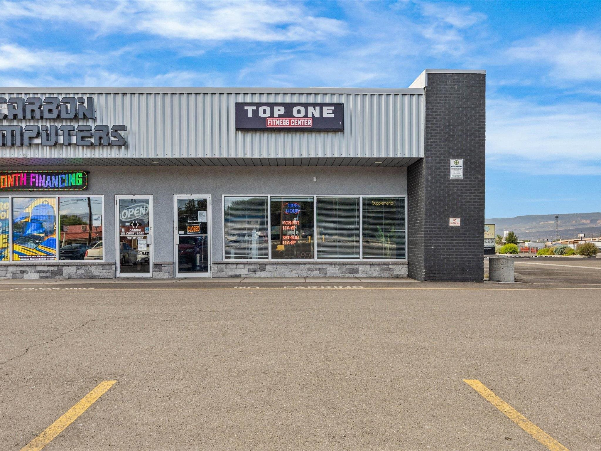 Commercial storefront with Carbon Computers and Top One Fitness Center signs and parking spaces in front.