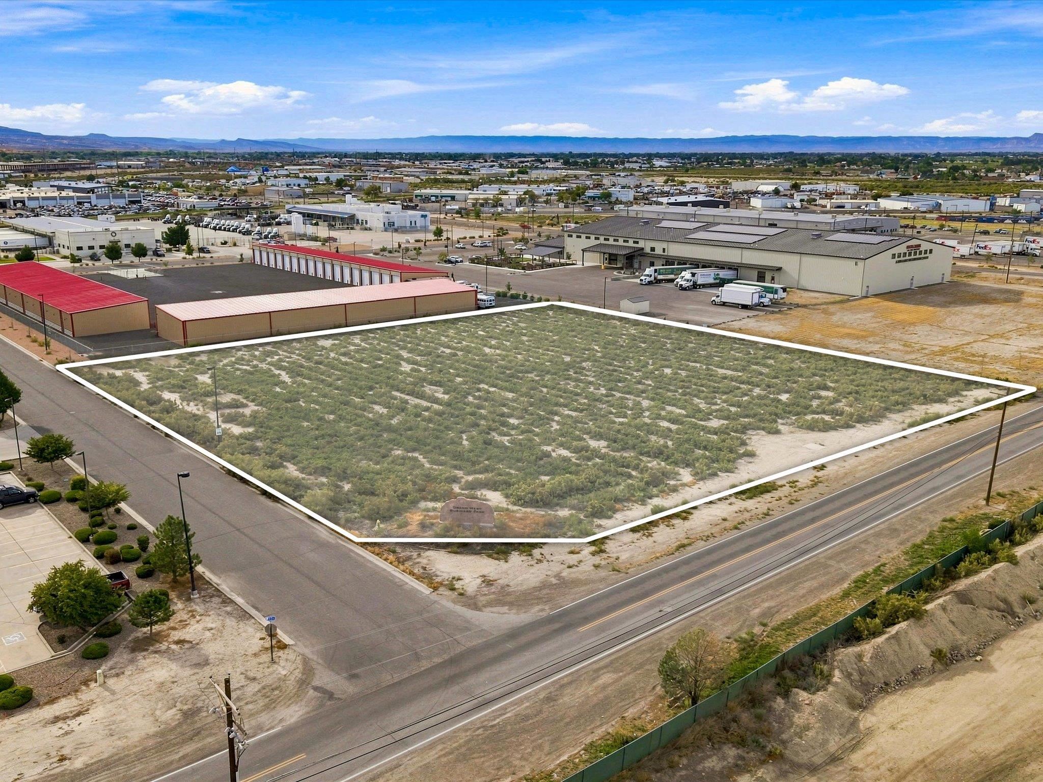 Vacant commercial lot outlined in white beside warehouses, a road, and railway tracks.