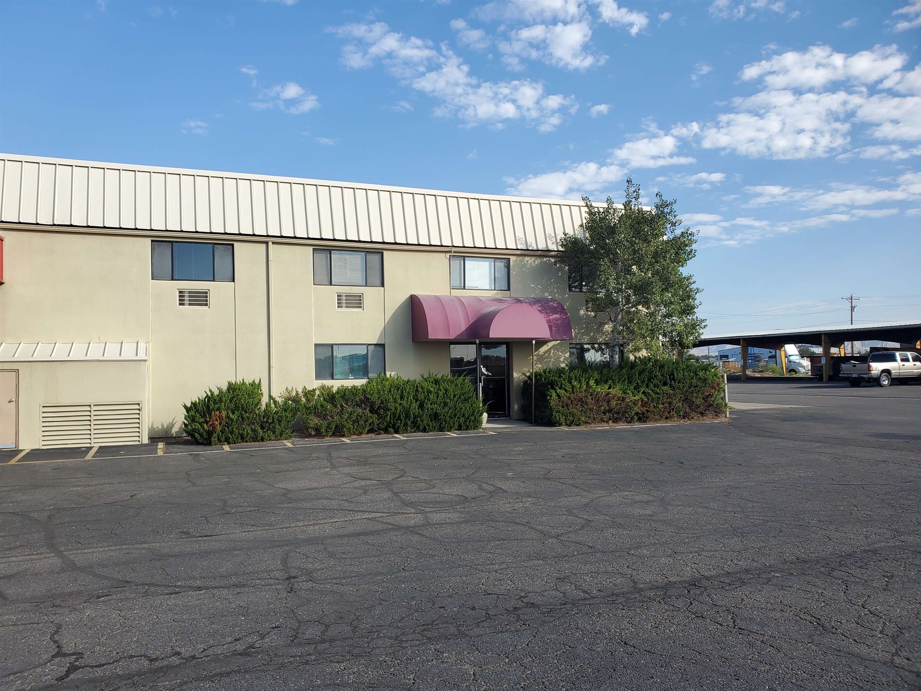 Commercial building with a burgundy entrance awning, shrubs, and a paved parking lot.