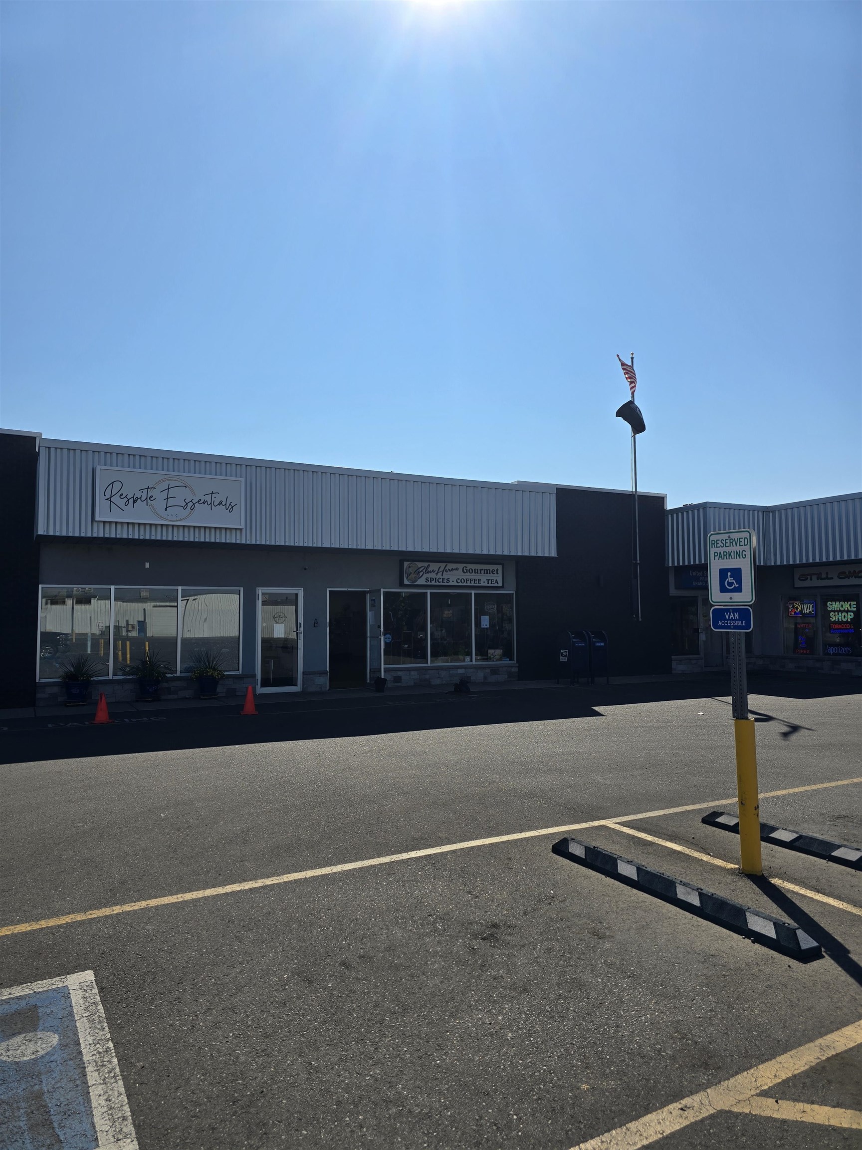 Commercial strip storefronts with an American flag and accessible parking spaces in front.