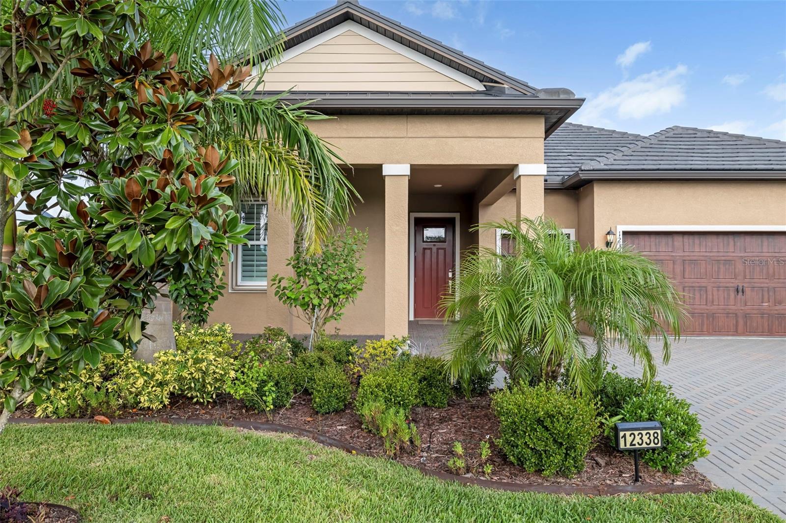 Home exterior with a covered entry, tropical landscaping, paver driveway, and wood-look garage door.