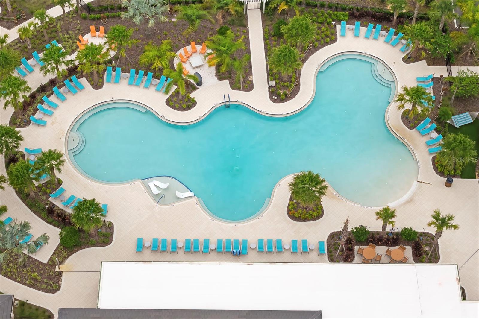 Aerial view of a freeform community pool surrounded by turquoise lounge chairs and tropical landscaping.