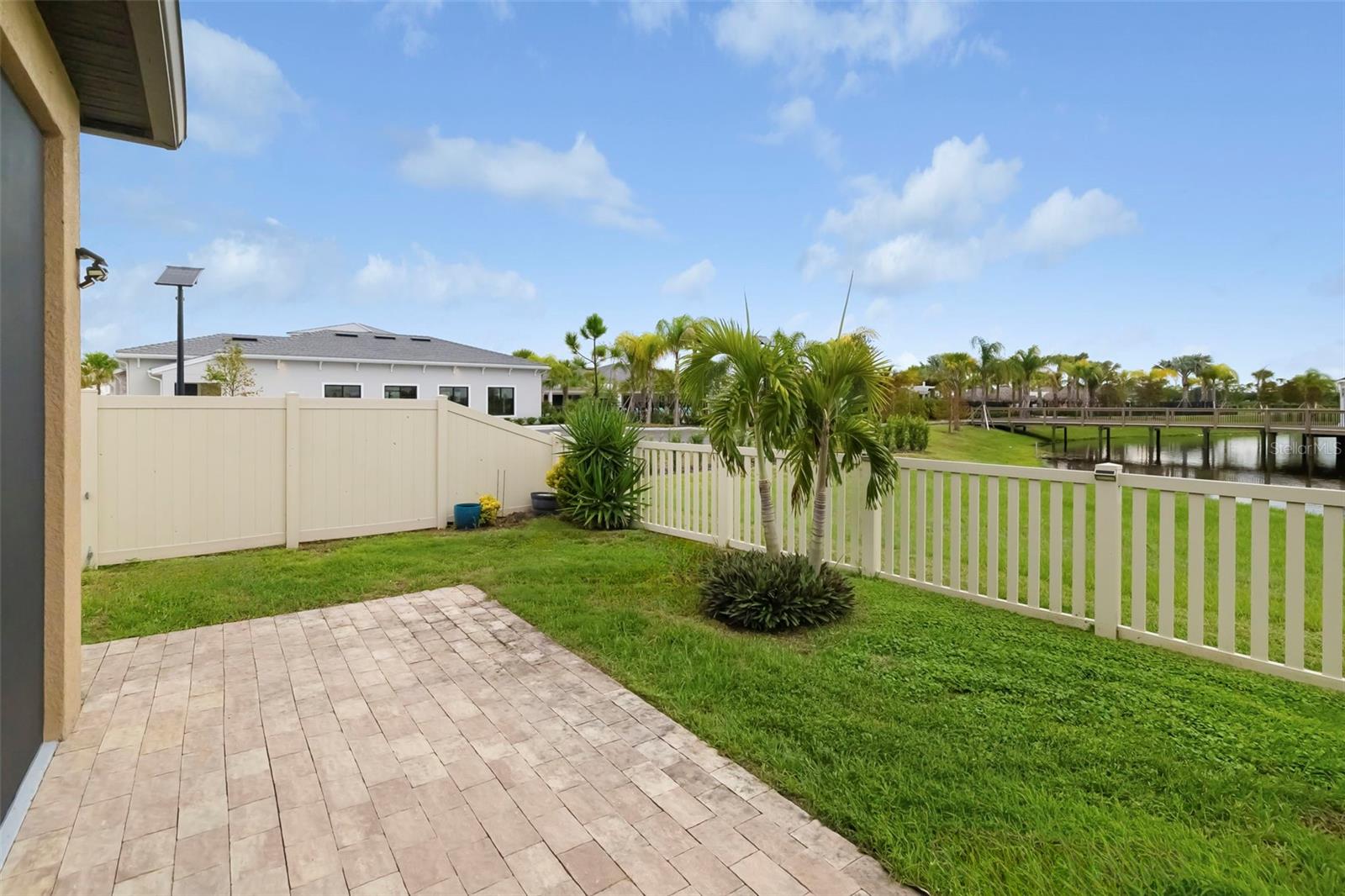 Backyard patio and fenced lawn overlooking a pond and pedestrian bridge.