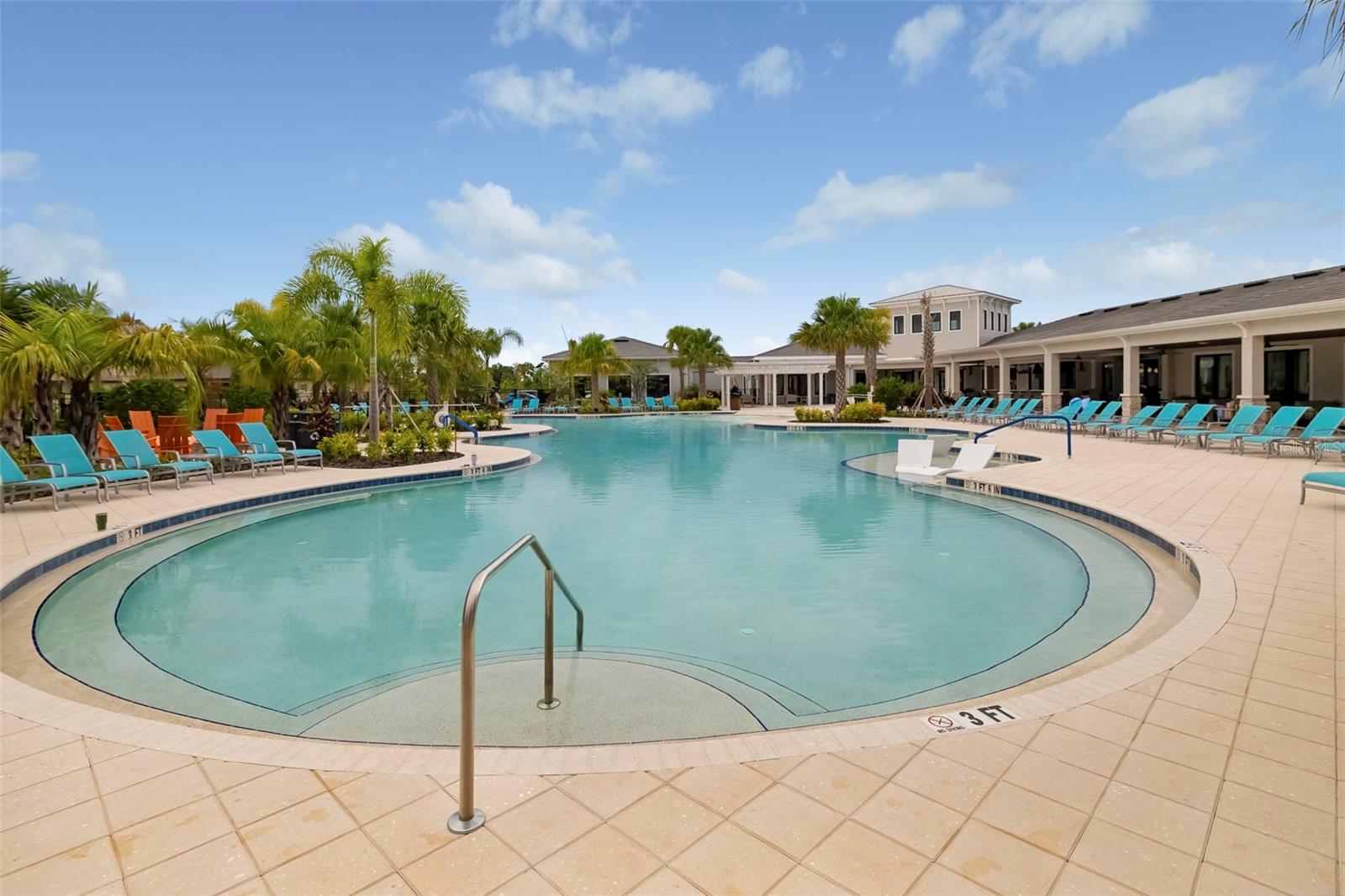 Community pool with a shallow-entry area, turquoise lounge chairs, palm trees, and a covered clubhouse.