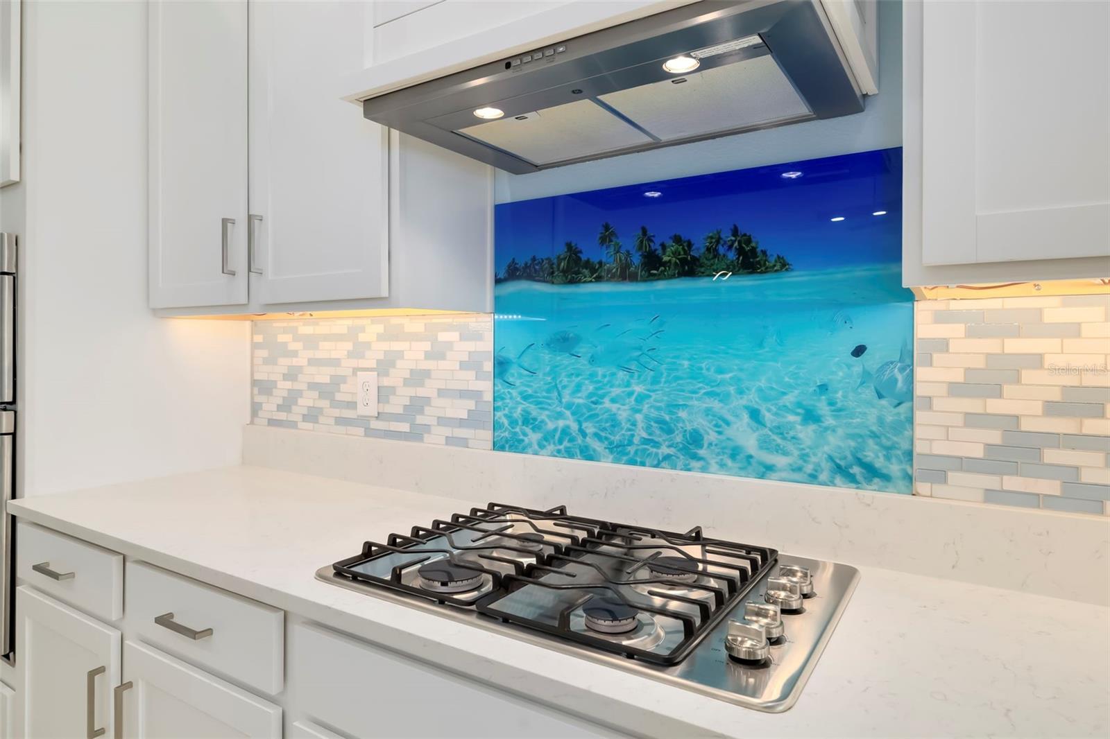Kitchen with a gas cooktop and a vivid blue tropical island backsplash mural.