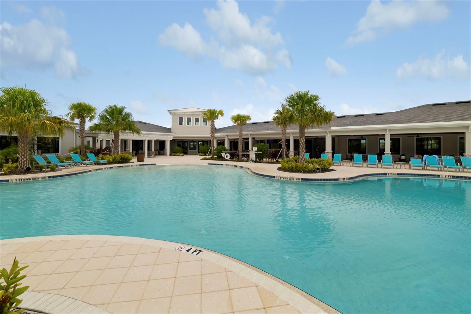 Outdoor pool beside a clubhouse, with palm trees and turquoise lounge chairs.
