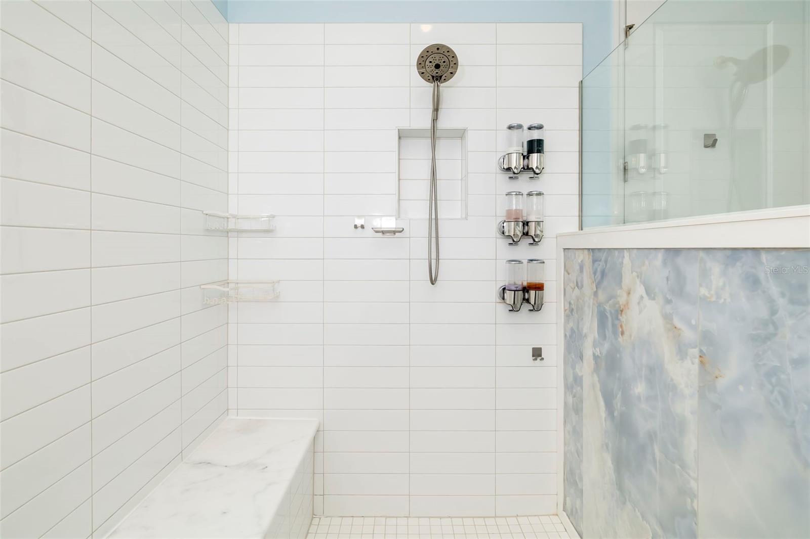Walk-in shower with white tile, a built-in bench, and a glass enclosure with a blue-gray patterned panel.