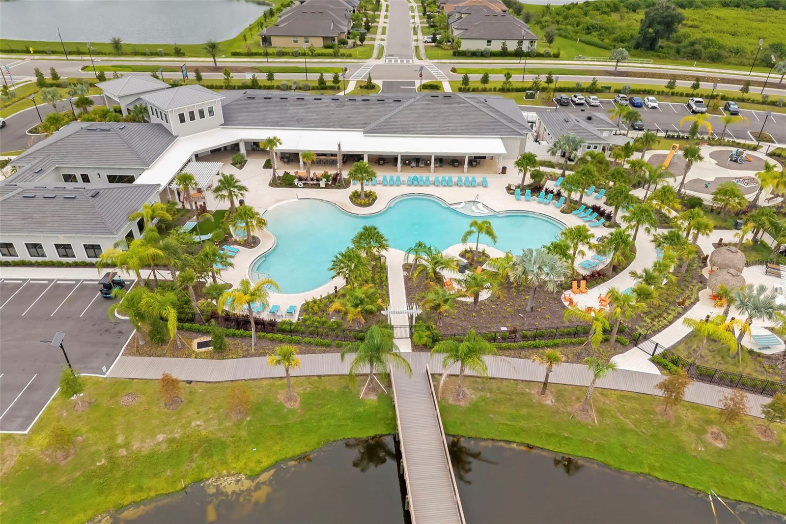 Aerial view of a community pool and clubhouse with a playground and landscaped grounds.