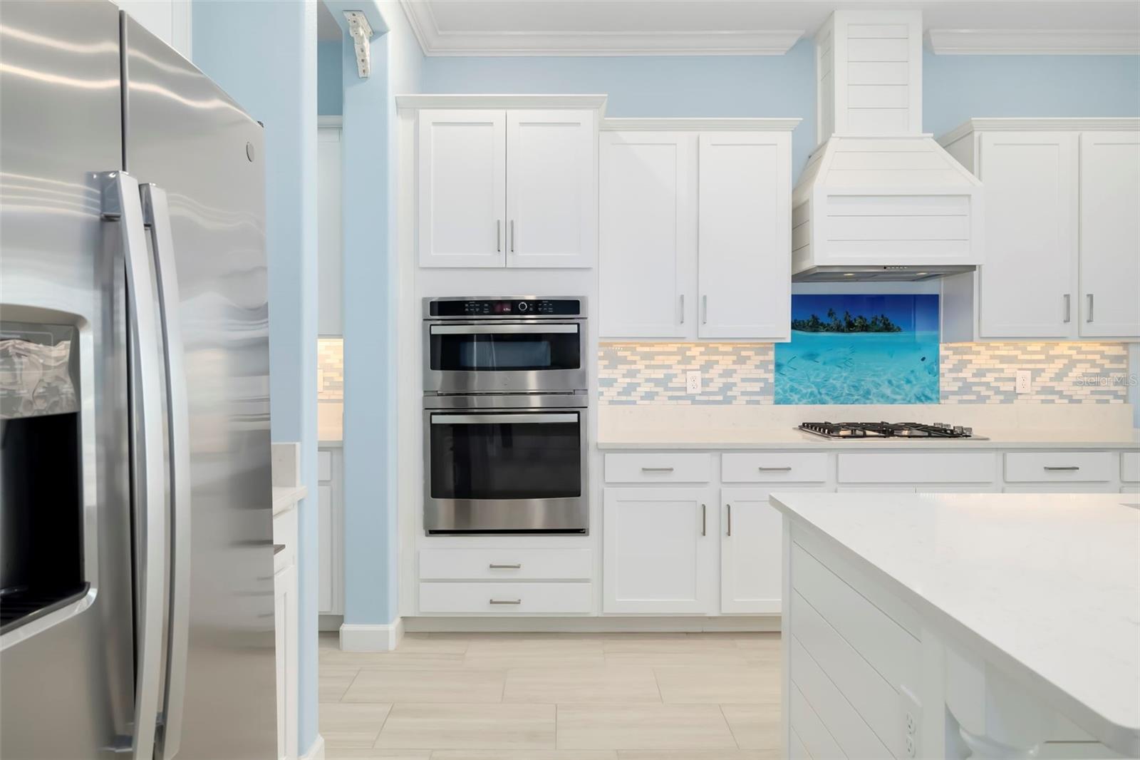 Kitchen with white cabinetry, stainless-steel double ovens, a large island, and an ocean-themed backsplash.
