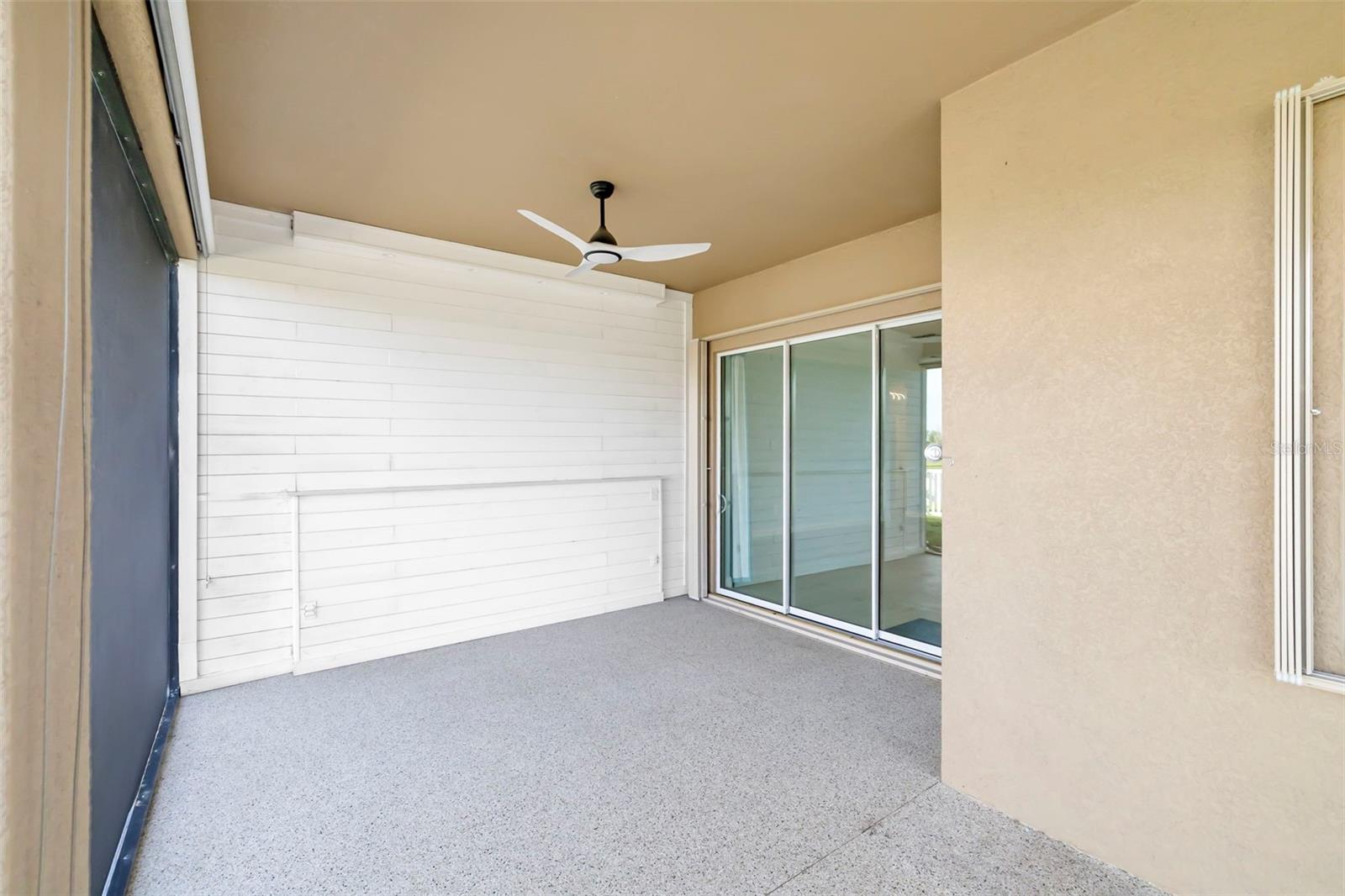 Covered patio with a ceiling fan, white siding, and sliding glass doors.