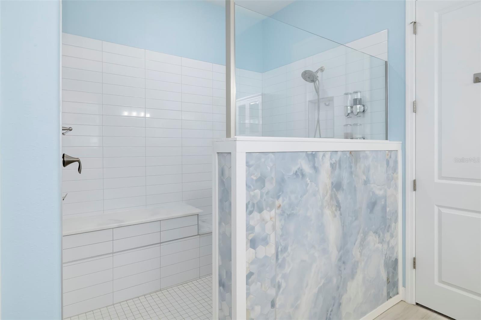 Bathroom with a glass walk-in shower, tiled bench, and blue-gray patterned half-wall.