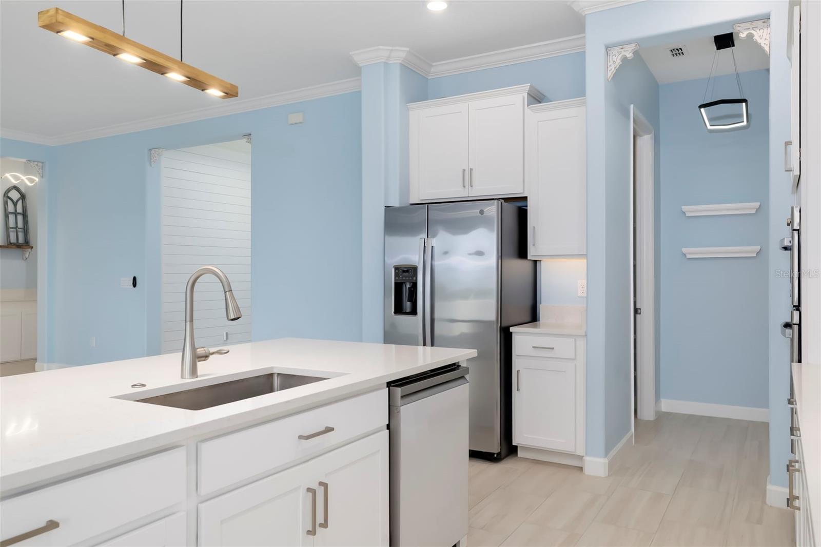 Kitchen with a white island sink, pale blue walls, and stainless steel refrigerator.