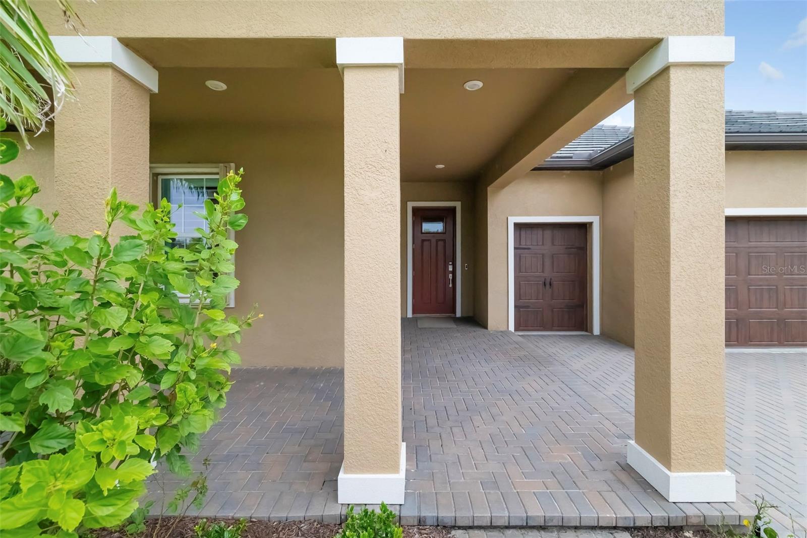 Tan stucco home with a covered entry, red front door, and brick-paver driveway.