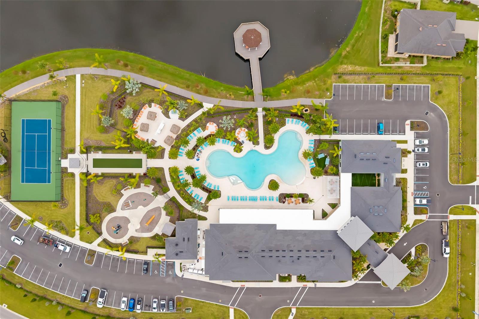 Aerial view of a community amenity center with a pool, tennis court, and lake dock.