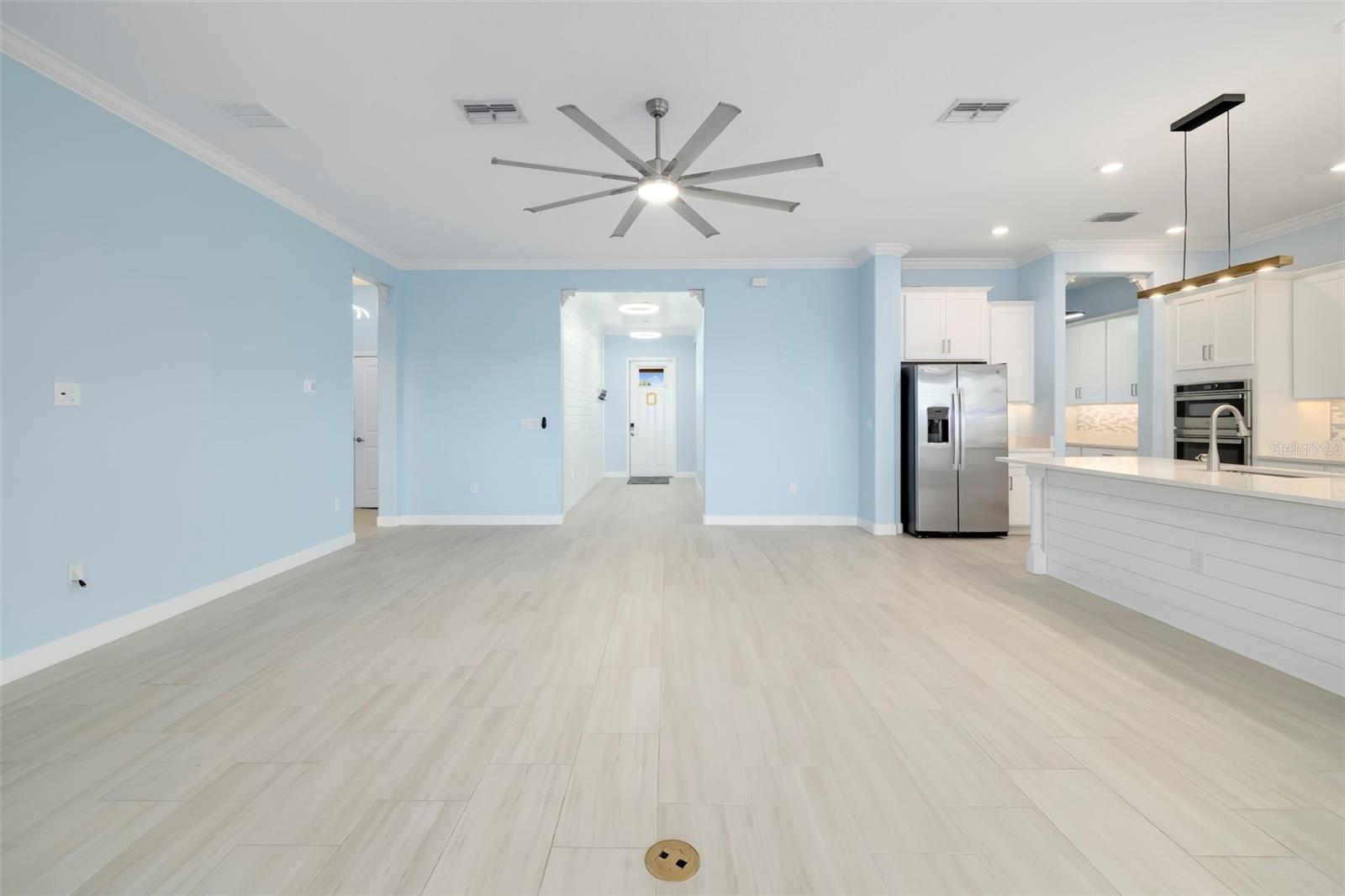 Unfurnished living area opening to a white kitchen with an island and stainless steel appliances.