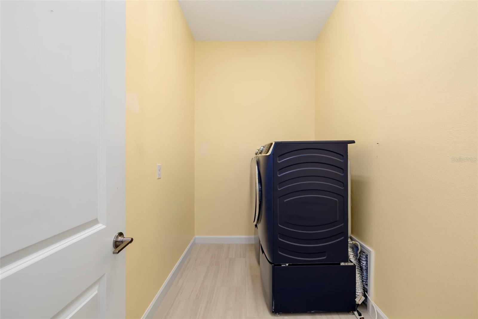 Laundry room with a dark appliance, pale yellow walls, and light wood-look flooring.