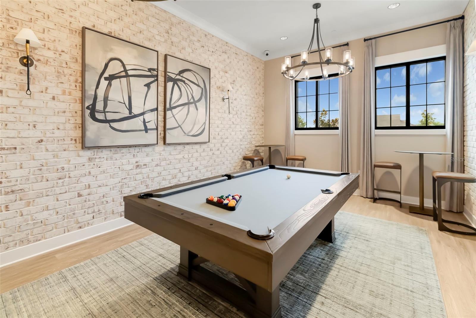 Game room with a pool table, white brick wall, abstract art, and tall black-framed windows.