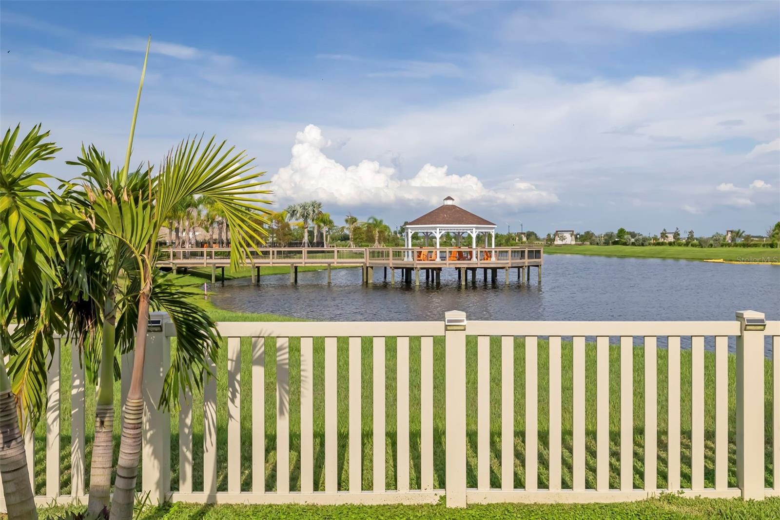 Community pond with a boardwalk and gazebo, framed by palm trees and a cream railing.
