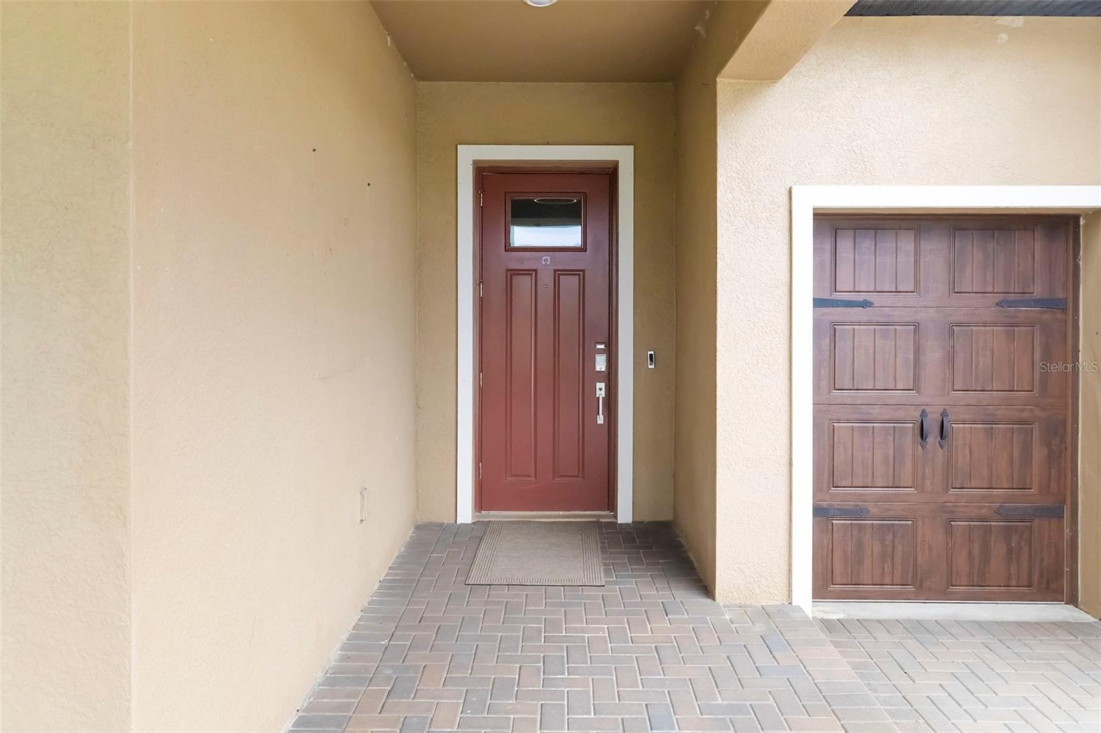 Covered home entry with a red front door and wood-look garage door.