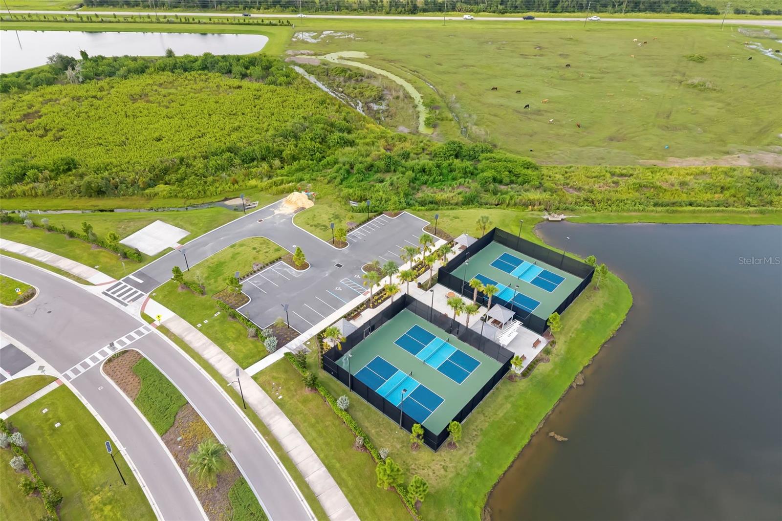 Aerial view of two fenced tennis courts beside a pond and landscaped community roads.