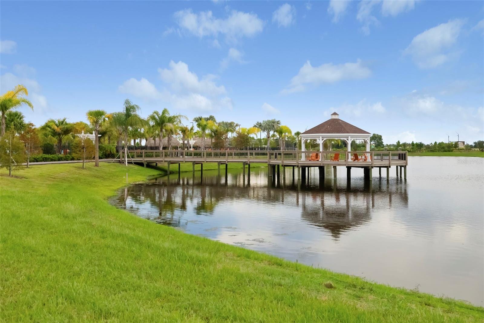 Lakefront boardwalk and gazebo beside palm trees and a grassy shore.
