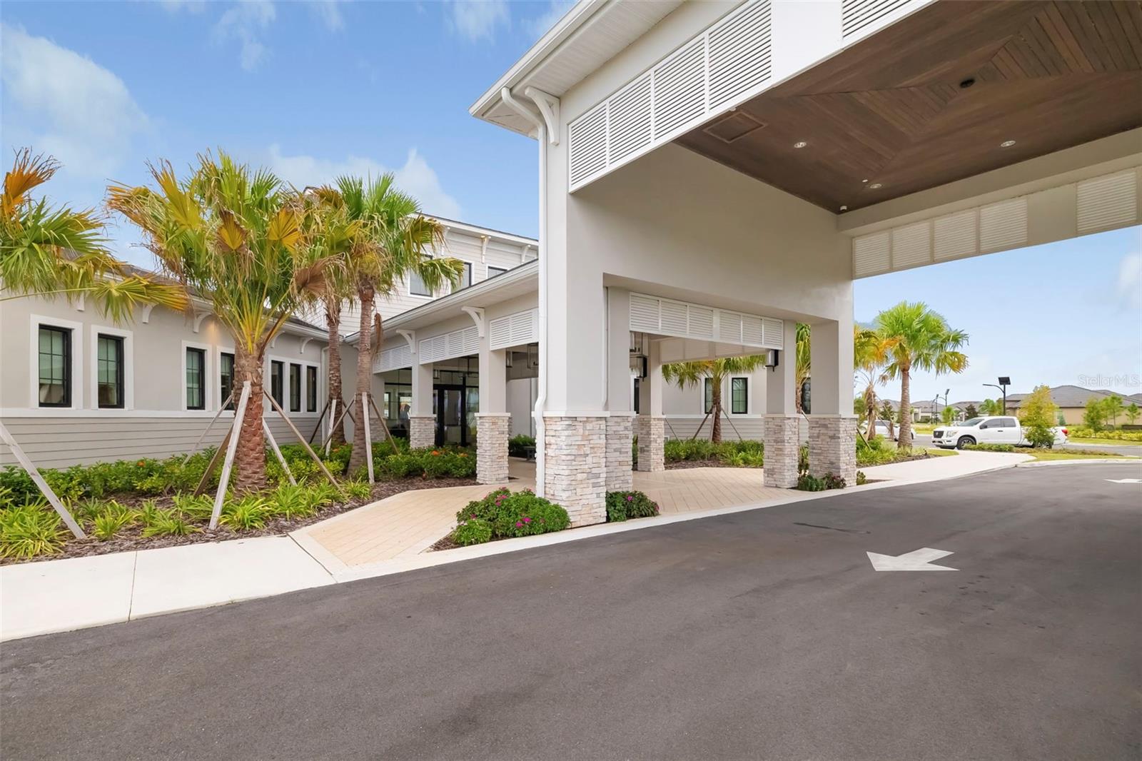 Building entrance with a broad covered drop-off canopy, stone columns, and palm trees.